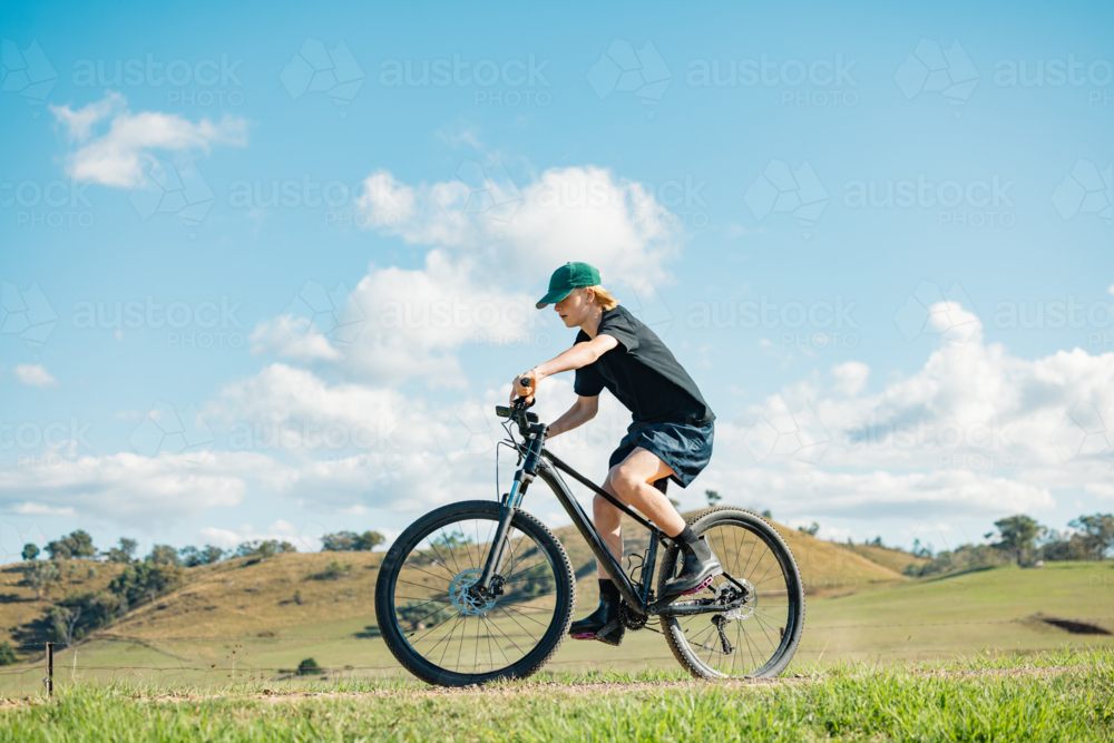 Teenage boy riding mountain bike on remote country road - Australian Stock Image