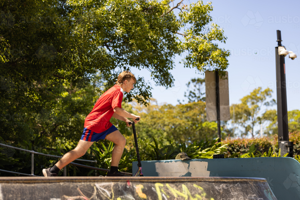 Image of Teenage boy riding scooter on ramps at skate park - Austockphoto