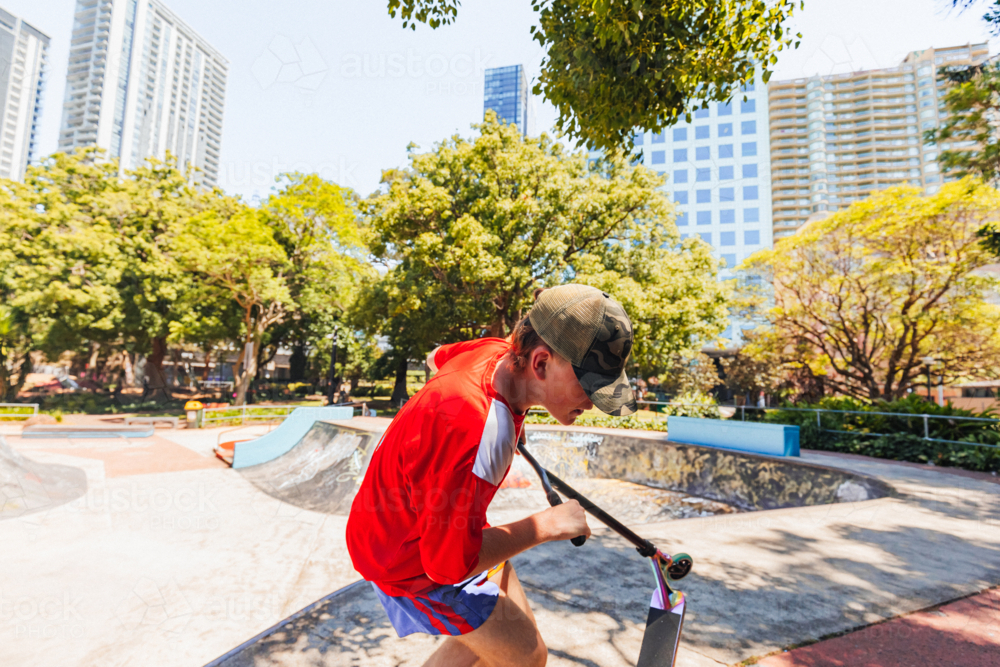 Teenage boy riding scooter on ramps at skate park - Australian Stock Image