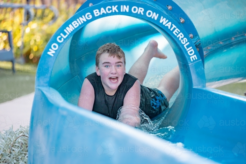 Teenage boy sliding down waterslide on holiday at caravan park - Australian Stock Image