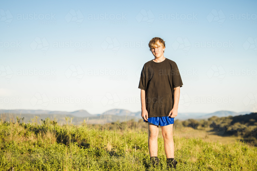 Teenage boy standing on high remote ridge line with hills in background - Australian Stock Image