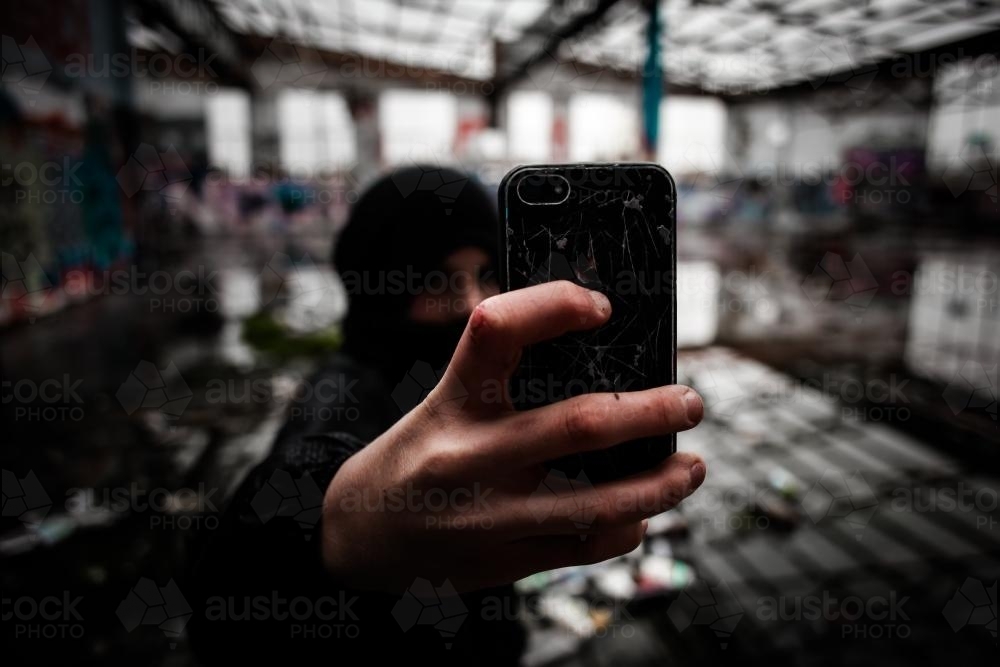 Teenage boy taking a picture on his mobile phone in deserted warehouse - Australian Stock Image