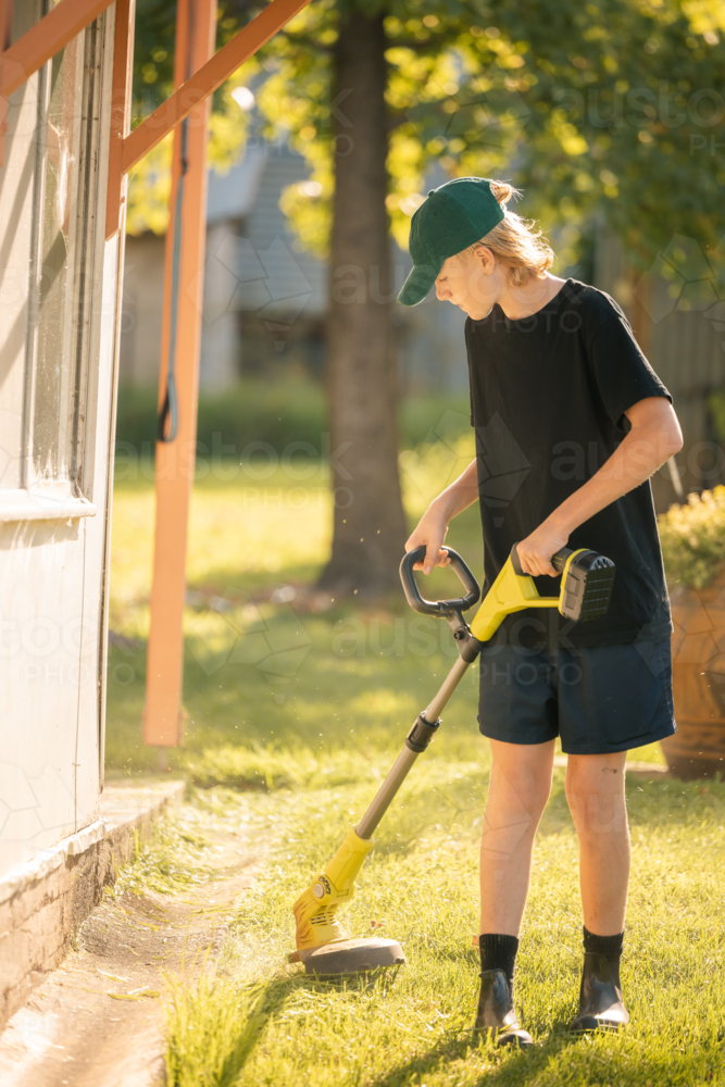 Teenage boy using line trimmer on lawn edging in country garden - Australian Stock Image