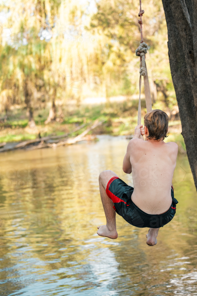 Boy Using A Rope Image of Teenage boy using rope swing at the river - Austockphoto
