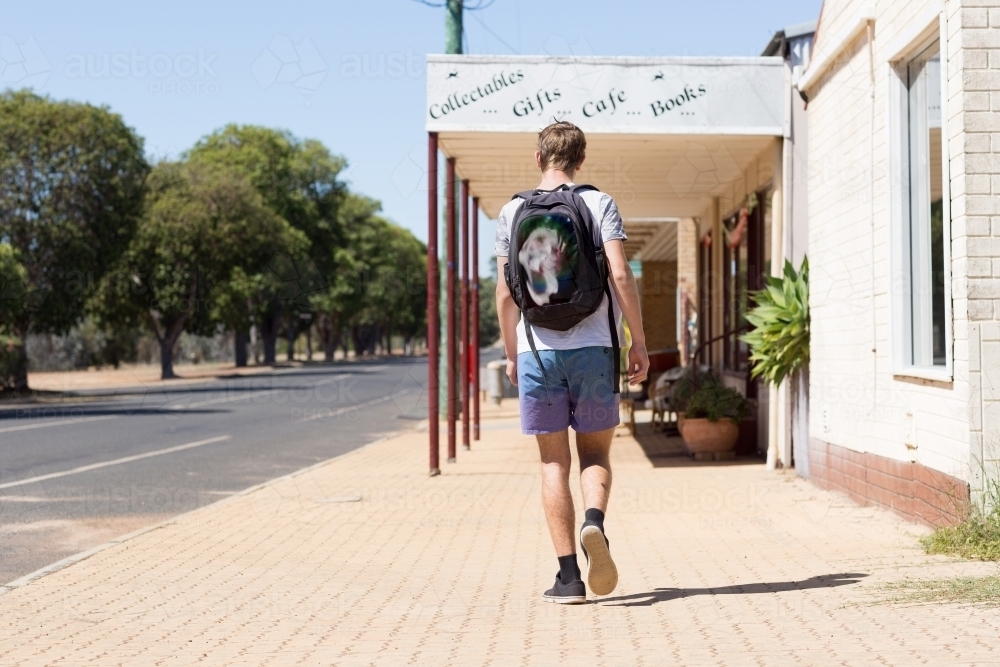 Teenage boy walking down a deserted street in a small town - Australian Stock Image