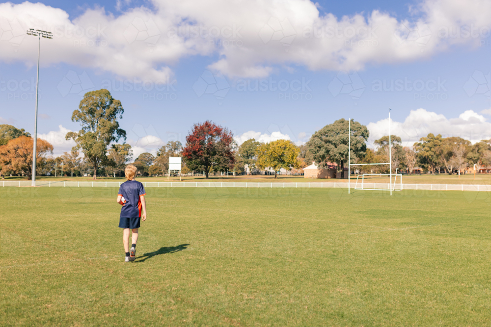 Teenage boy walking on empty rugby field towards goal posts - Australian Stock Image