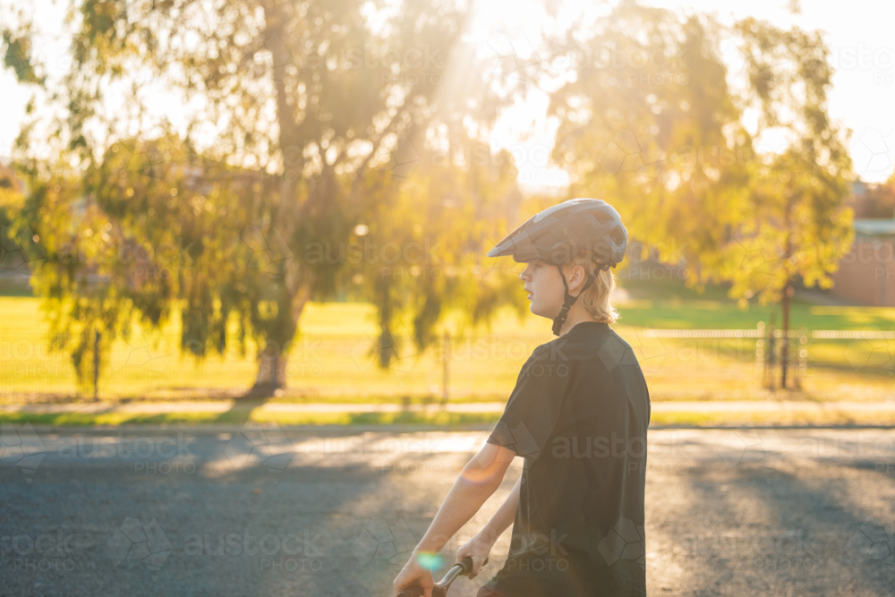 Teenage boy wearing helmet riding scooter in the street - Australian Stock Image