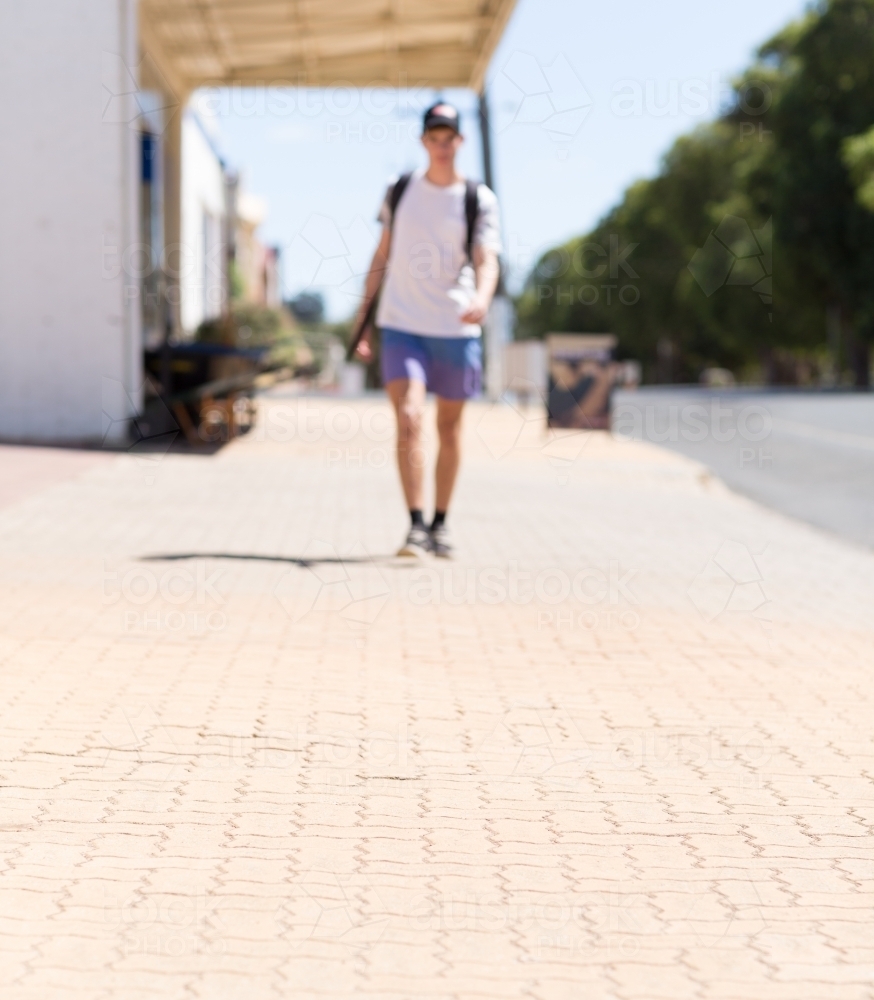 Teenage boy with backpack walking down paved footpath - Australian Stock Image