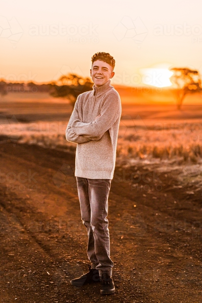 Teenage boy with folded arms on rural dirt road at sunset - Australian Stock Image