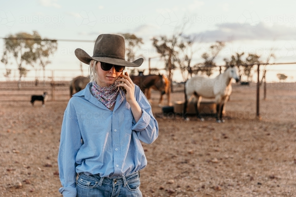 Teenage country woman on her phone standing in the horse yard - Australian Stock Image
