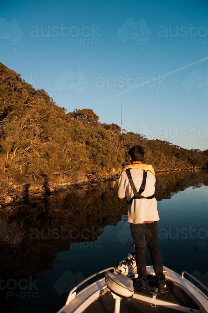 Teenage fisherman standing in boat on river - Australian Stock Image