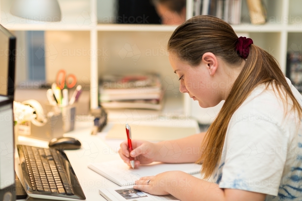 Teenage girl at desk writing notes - Australian Stock Image