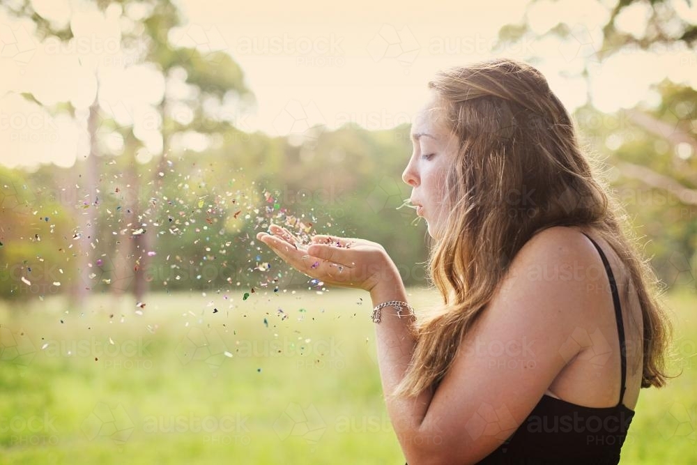 Teenage girl blowing confetti in a field - Australian Stock Image