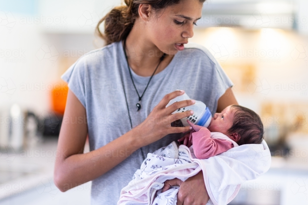 teenage girl feeding her infant baby sister with a bottle - Australian Stock Image