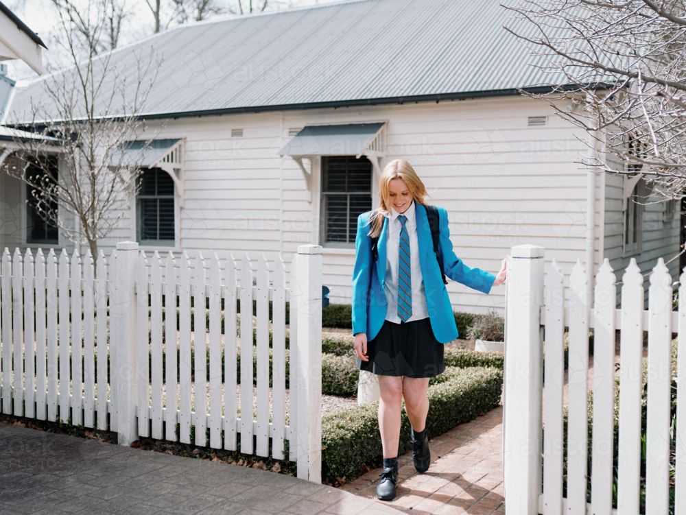 Teenage girl in blue uniform walking out of the picket fence of their new home - Australian Stock Image
