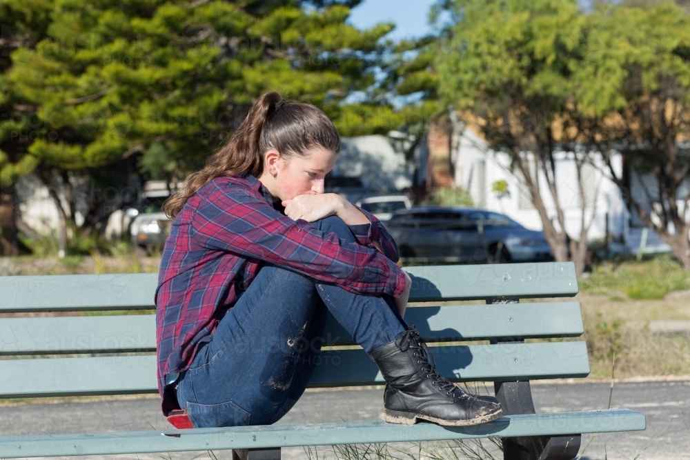 Teenage girl in pensive pose hugging her knees - Australian Stock Image