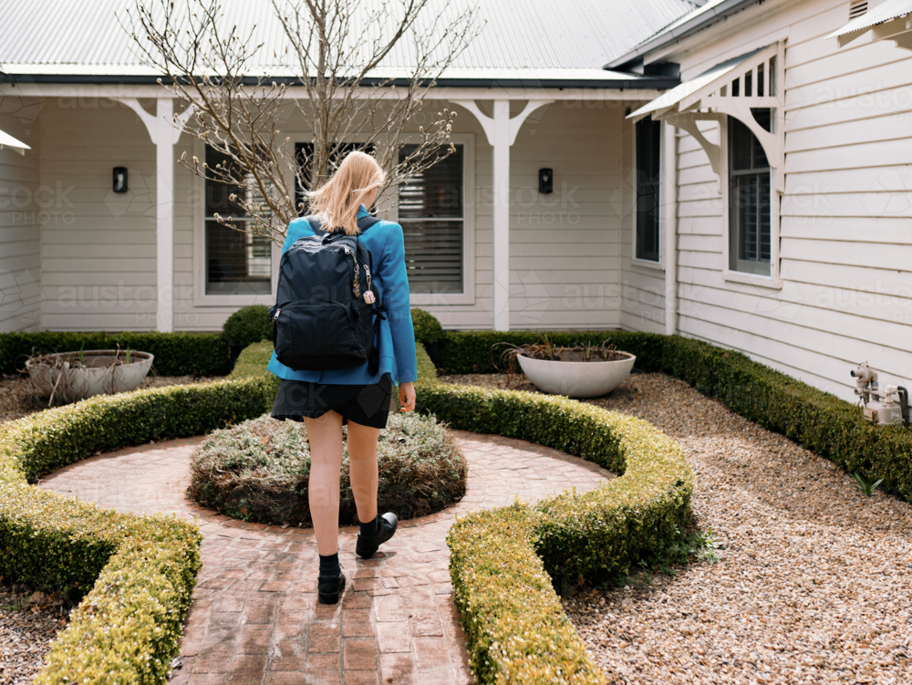 Teenage girl in school uniform walks along a curved brick path of their new home - Australian Stock Image