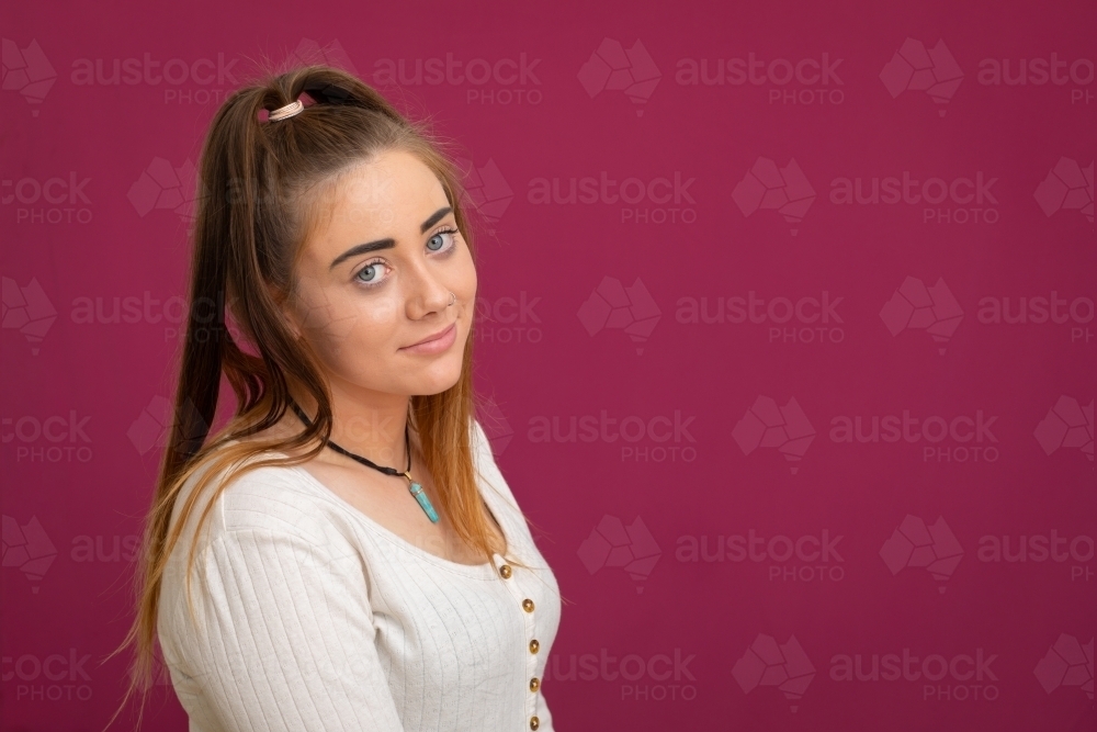 teenage girl looking resignedly at camera on magenta background - Australian Stock Image