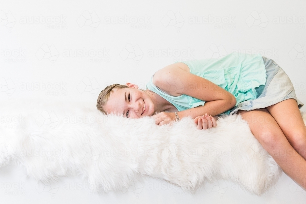 Teenage girl lying sideways on rug smiling - Australian Stock Image