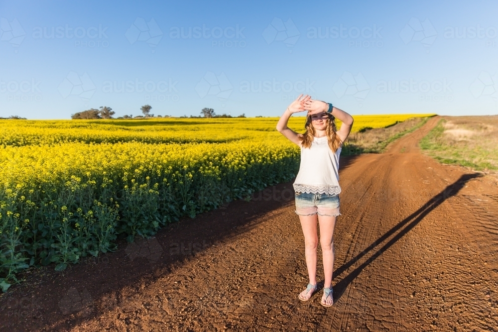Teenage girl on farm next to canola crop shielding eyes from sun - Australian Stock Image