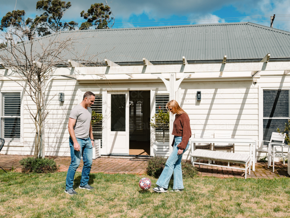 Teenage girl playing soccer ball with dad in the garden of their new home - Australian Stock Image
