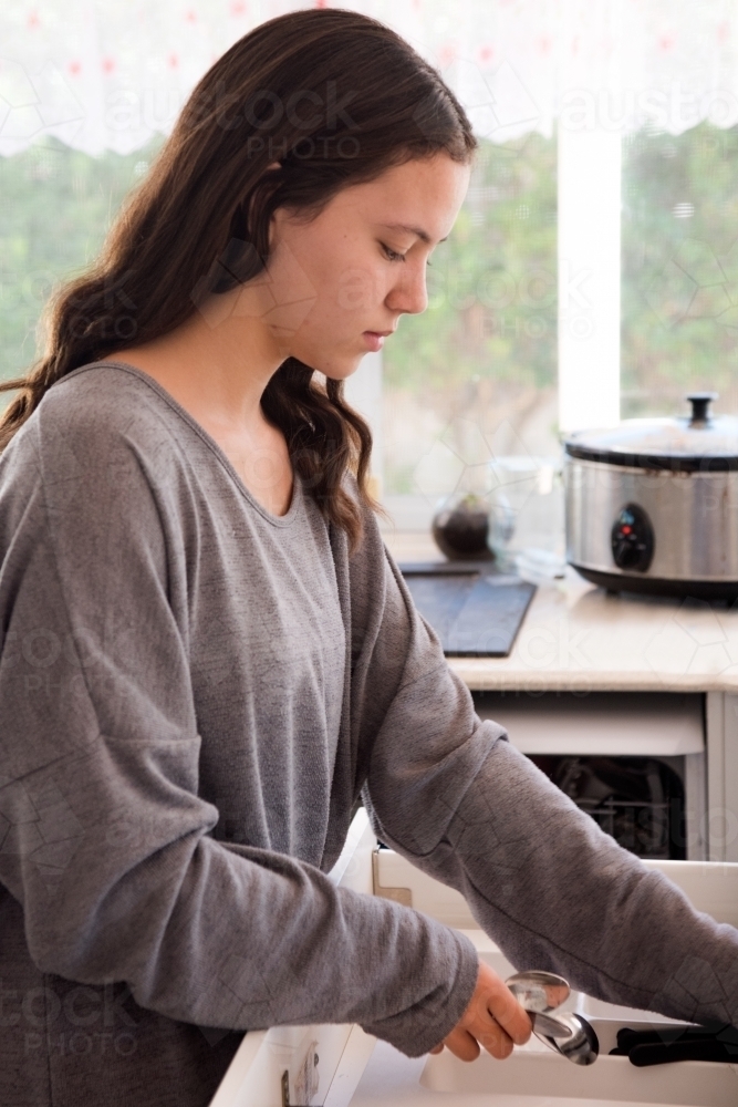 Teenage girl putting away cutlery. - Australian Stock Image