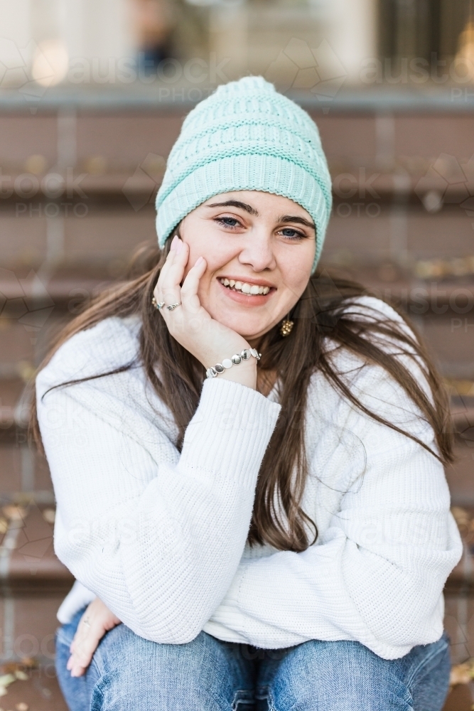 Teenage girl resting chin on hand smiling sitting at bottom of stairs - Australian Stock Image