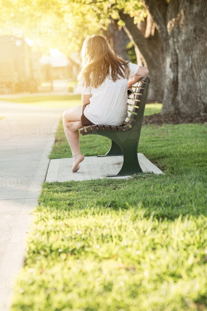 Teenage girl seated on park bench - Australian Stock Image