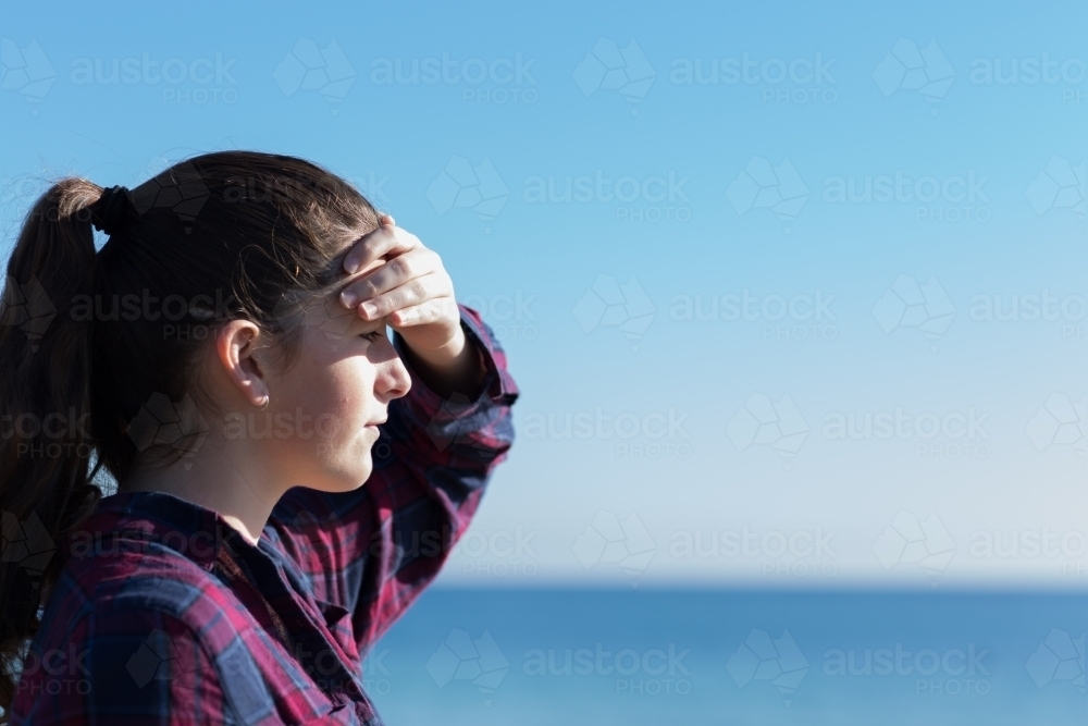 Teenage girl shading her eyes, looking out to sea - Australian Stock Image