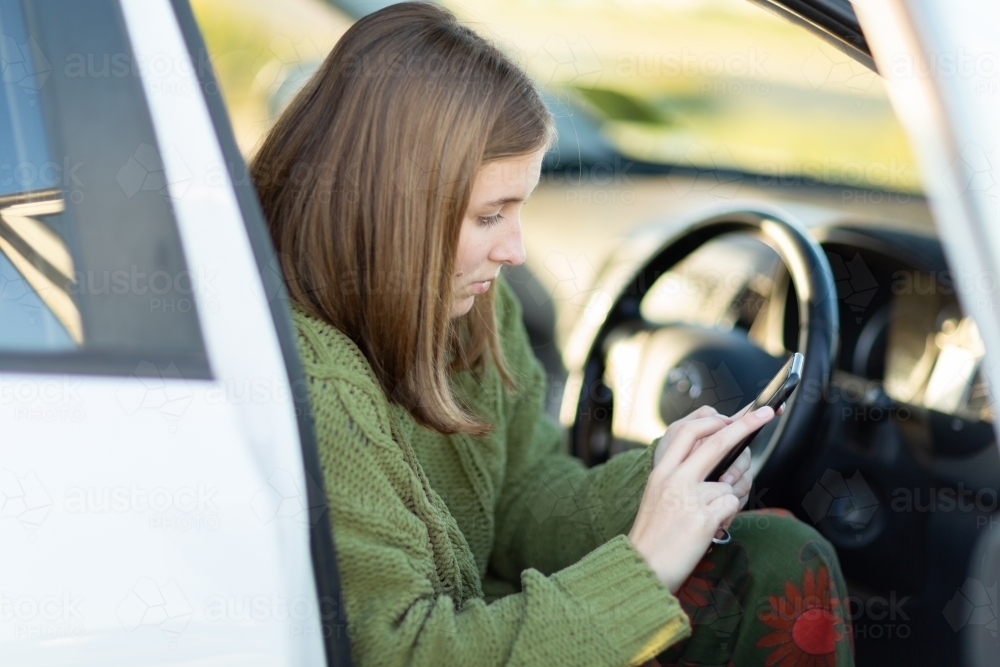 teenage girl sitting in drivers seat of car with phone - Australian Stock Image