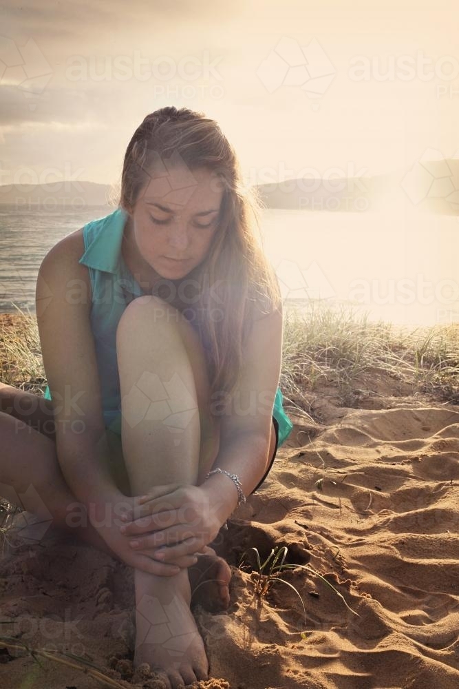 Teenage girl sitting on the beach at sunset - Australian Stock Image