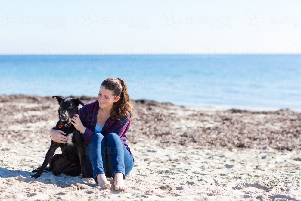 Teenage girl sitting on the beach with her dog - Australian Stock Image
