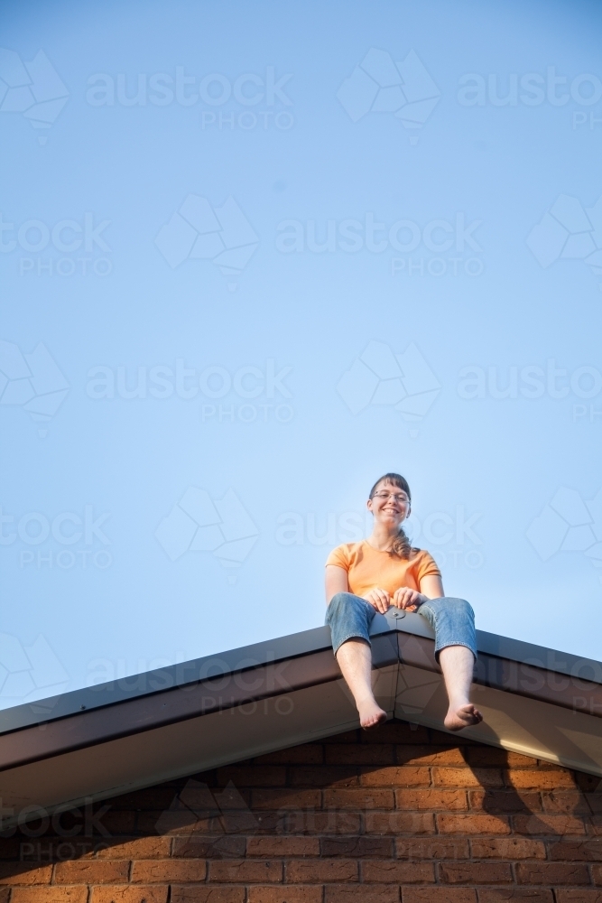 Teenage girl sitting on the house roof grinning - Australian Stock Image