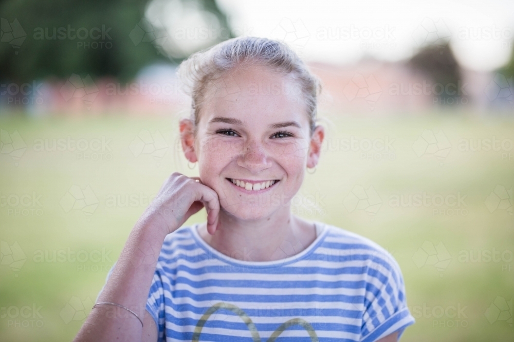Teenage girl sitting with hand near face smiling - Australian Stock Image