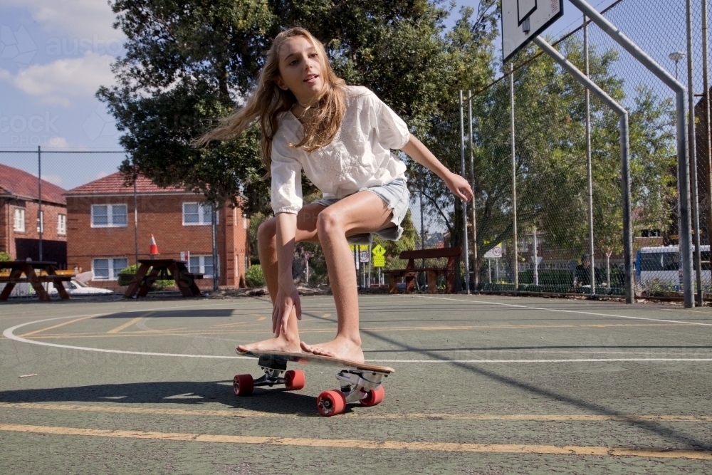 Teenage girl skateboarding in basketball court - Australian Stock Image