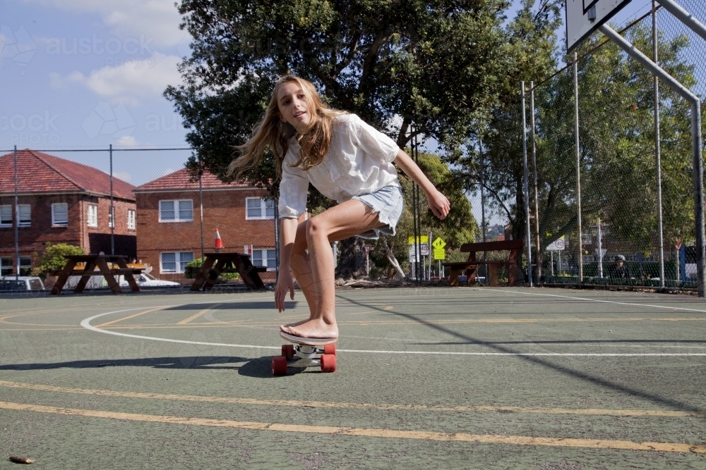 Teenage girl skateboarding in basketball court - Australian Stock Image