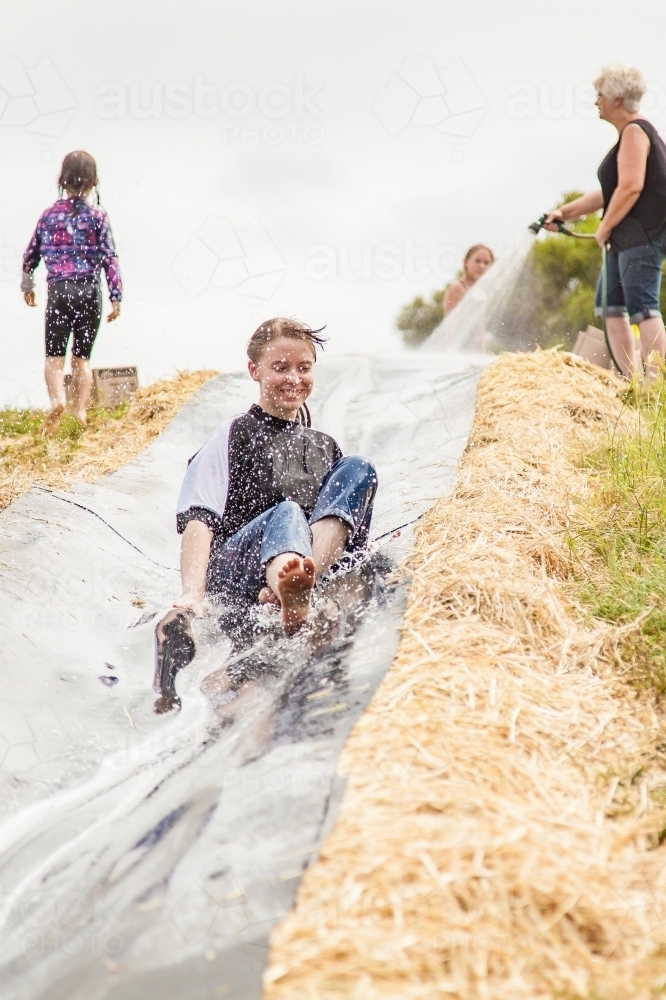 Teenage girl sliding down homemade water slide - Australian Stock Image