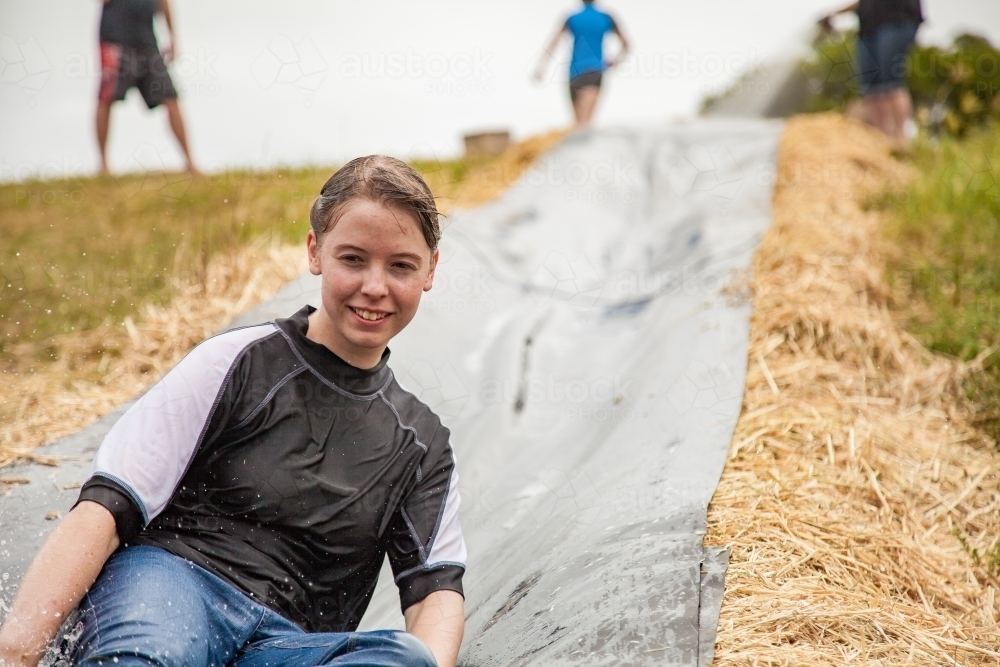 Teenage girl sliding down homemade water slide - Australian Stock Image