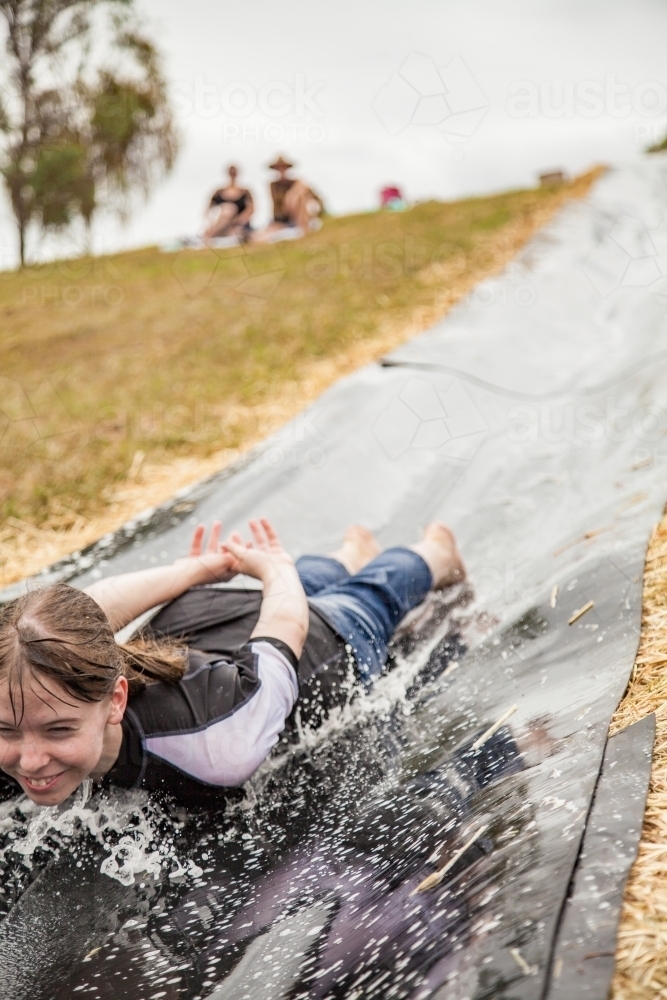 Teenage girl sliding down homemade water slide - Australian Stock Image