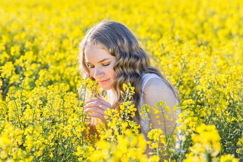 Teenage girl smelling canola flowers in paddock on farm - Australian Stock Image