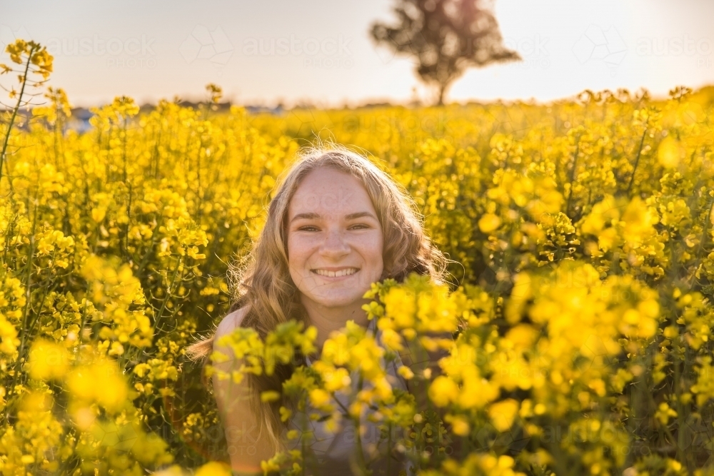 Teenage girl smiling among canola crop on farm - Australian Stock Image