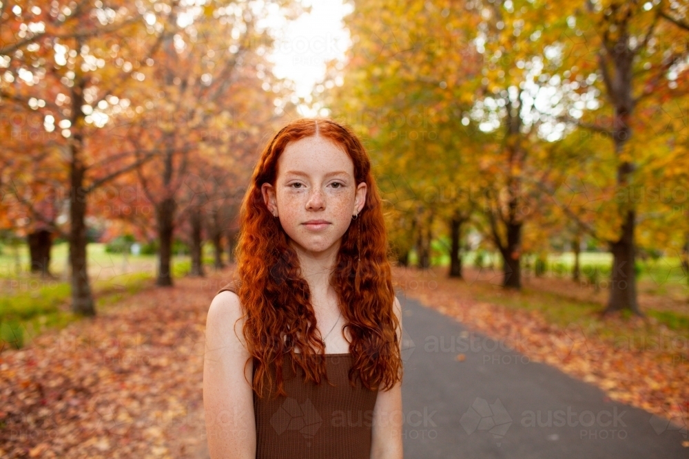 Teenage girl standing in a street lined with Autumn trees - Australian Stock Image