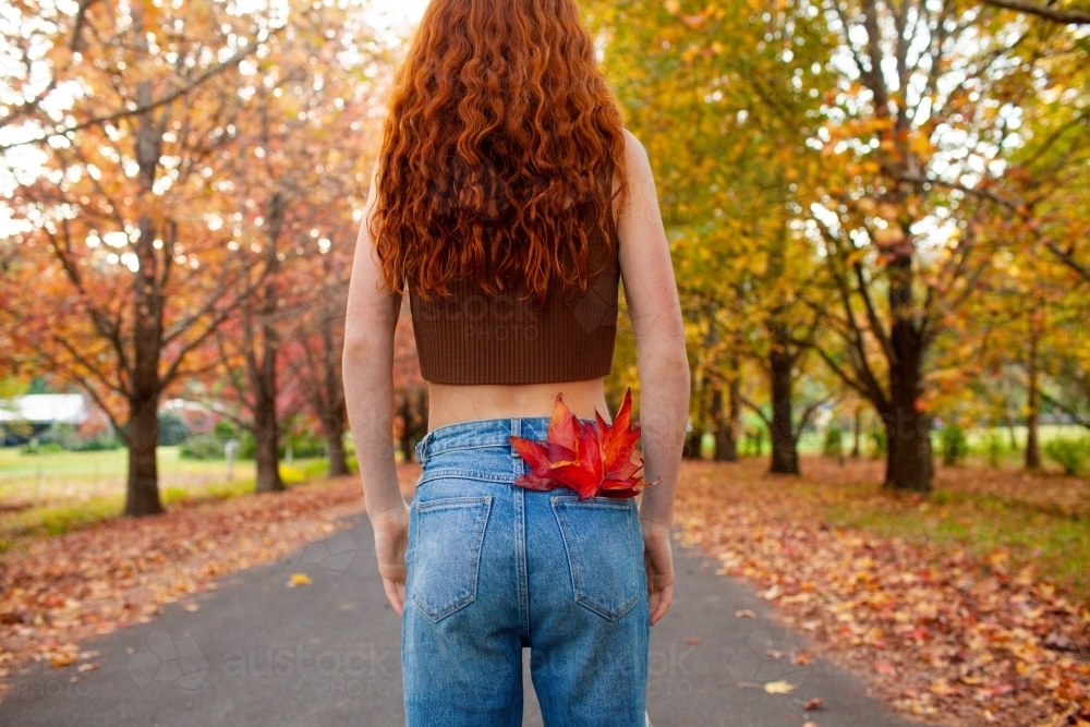 Teenage girl standing in a street lined with Autumn trees - Australian Stock Image