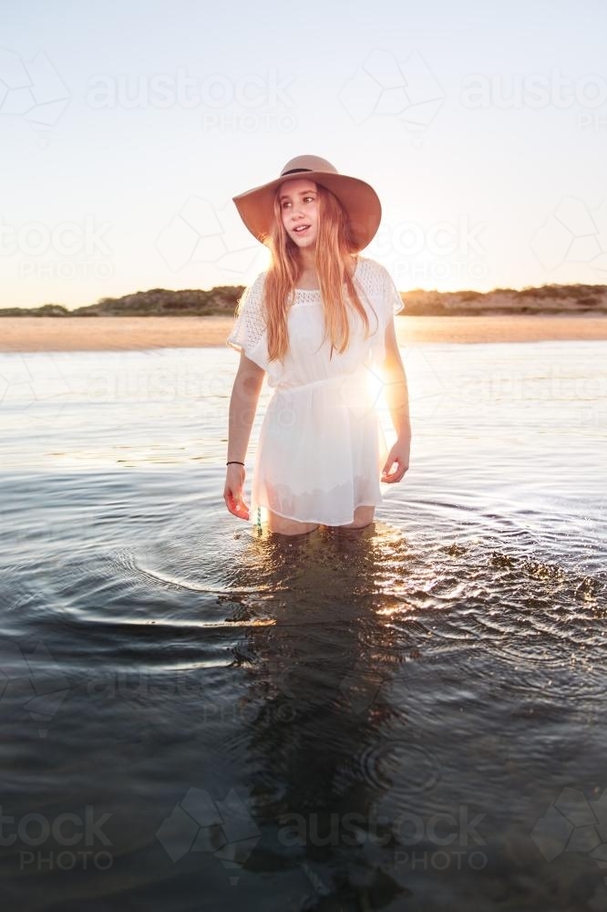 Teenage girl standing in calm water at the beach at sunset - Australian Stock Image