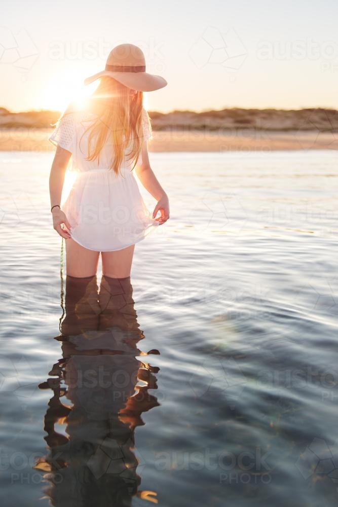Teenage girl standing in calm water at the beach at sunset - Australian Stock Image