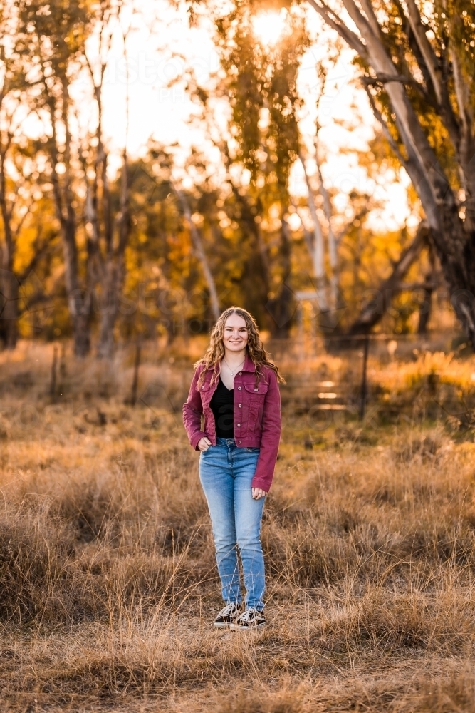 Teenage girl standing in long grass in paddock on farm - Australian Stock Image