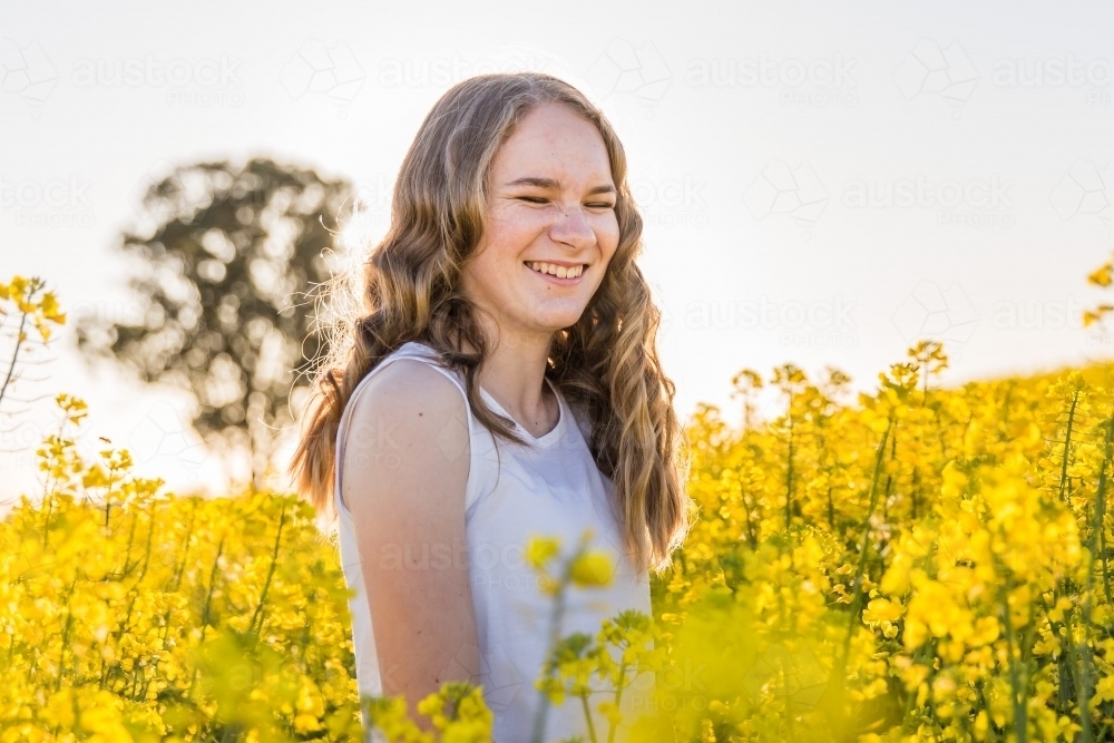 Teenage girl standing laughing in canola crop on farm - Australian Stock Image