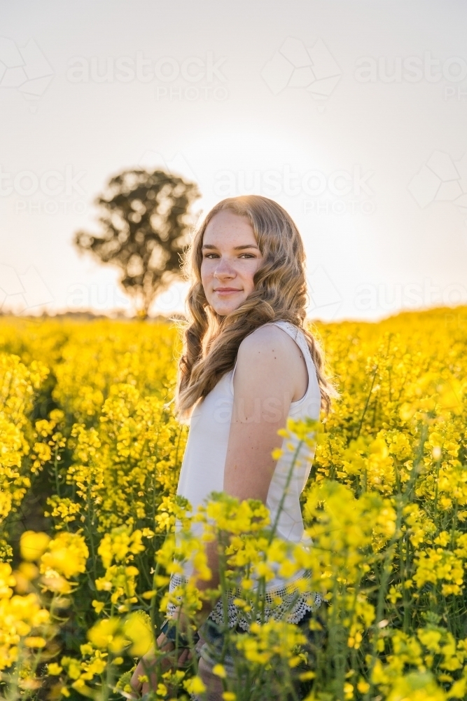 Teenage girl standing on farm in canola paddock - Australian Stock Image