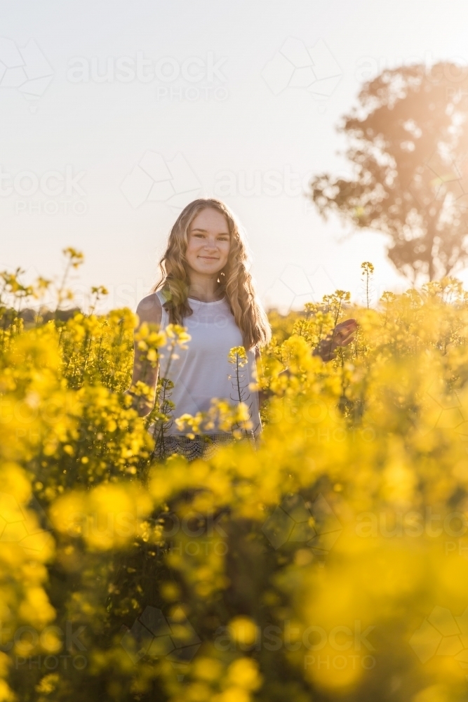 Teenage girl standing on farm in field of canola - Australian Stock Image