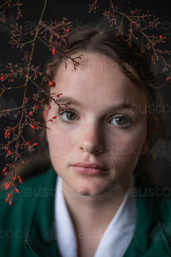 Teenage girl staring straight with red berries framing her face - Australian Stock Image